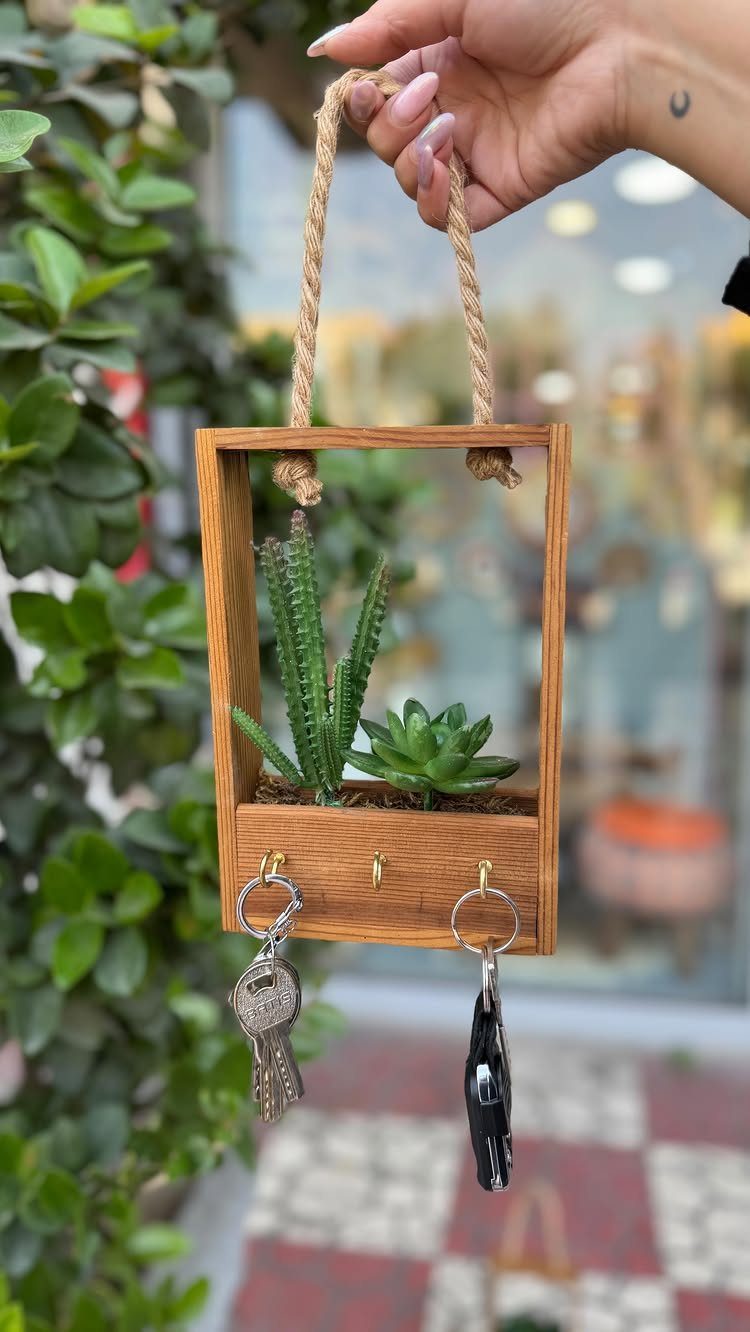 Wooden hanging key holder with small green succulents and two keys attached.