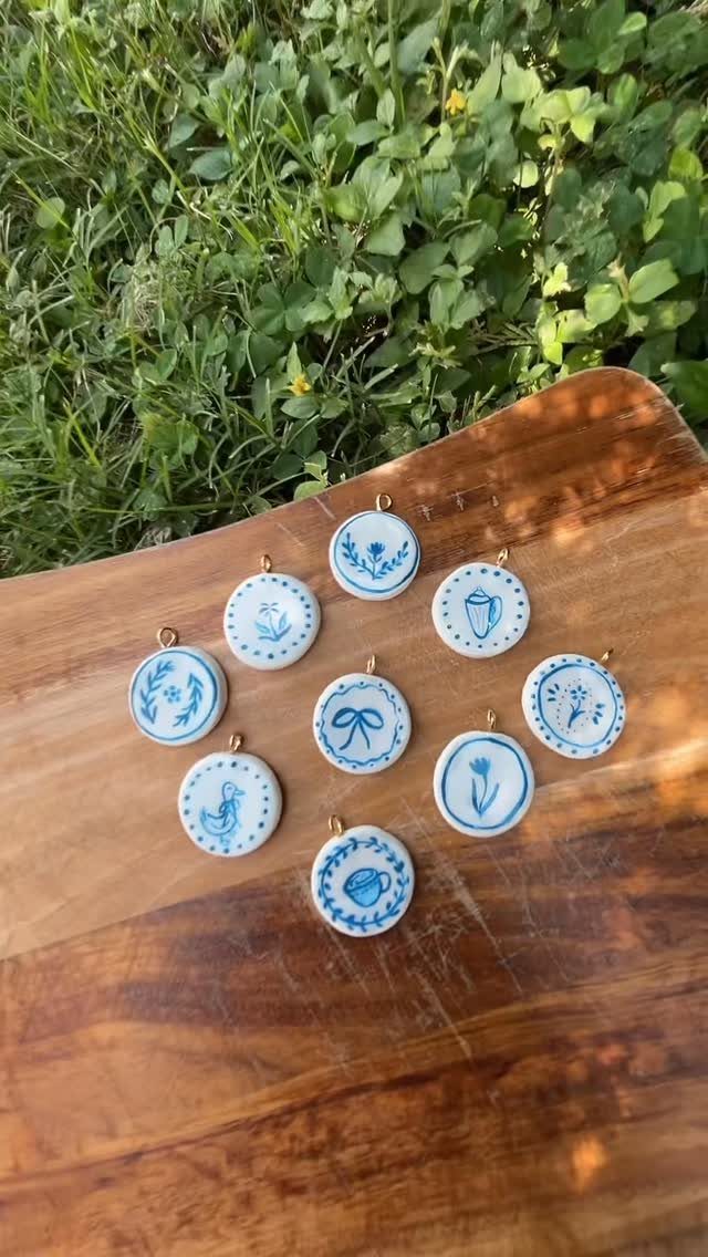 Round white clay pendants with blue floral designs on a wooden surface.