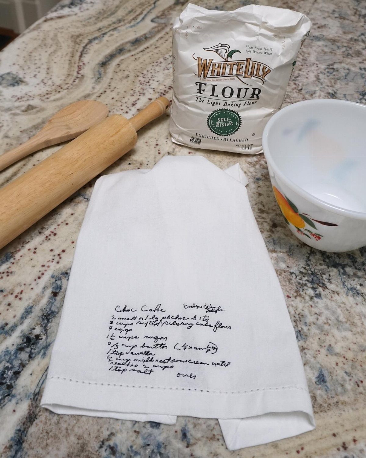 White tea towel with handwritten chocolate cake recipe next to baking ingredients
