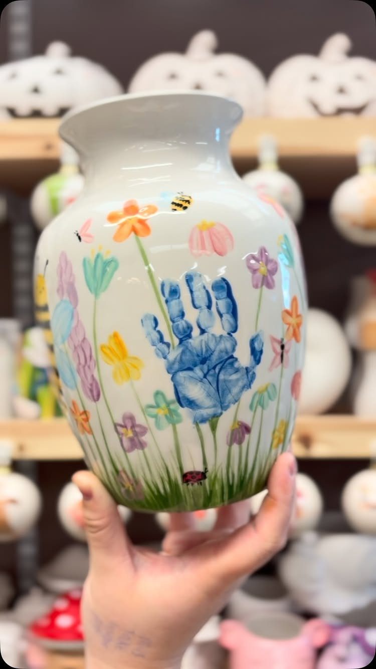 White ceramic vase painted with a blue handprint and colorful spring flowers.