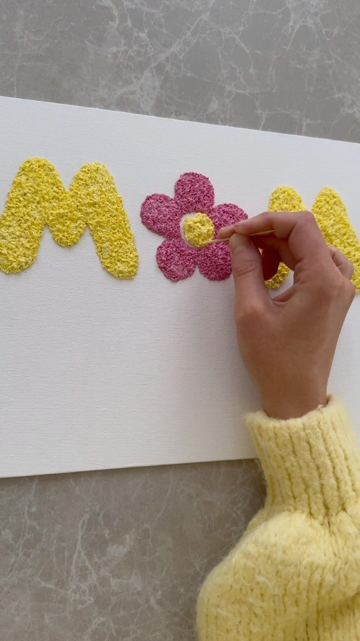 Hand painting the word MOM with textured yellow and pink paint on canvas