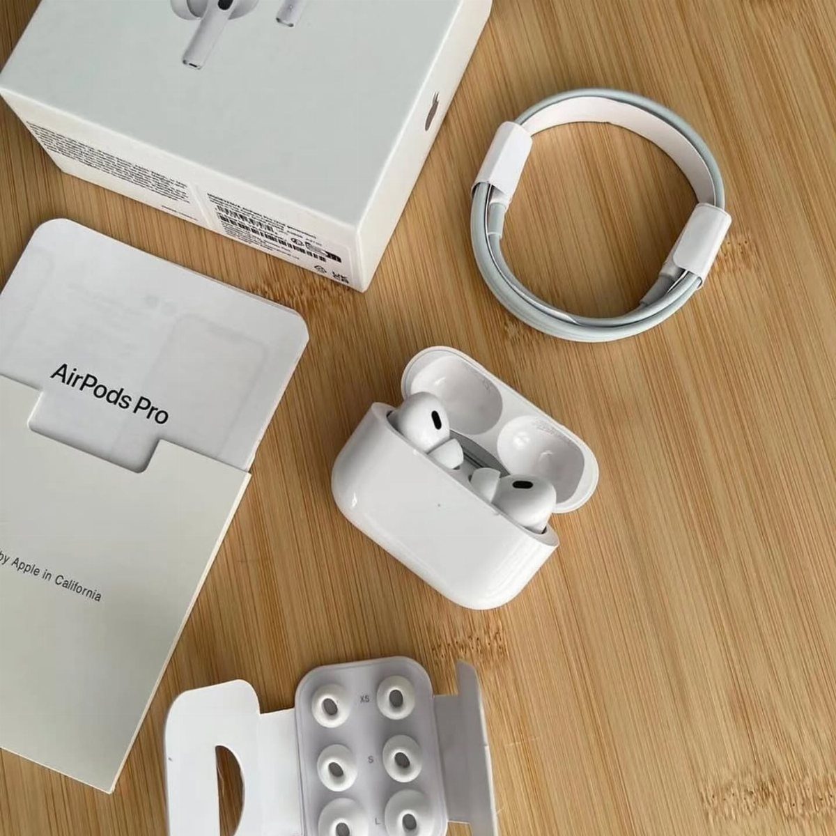 AirPods Pro earbuds in an open charging case with packaging on wooden table