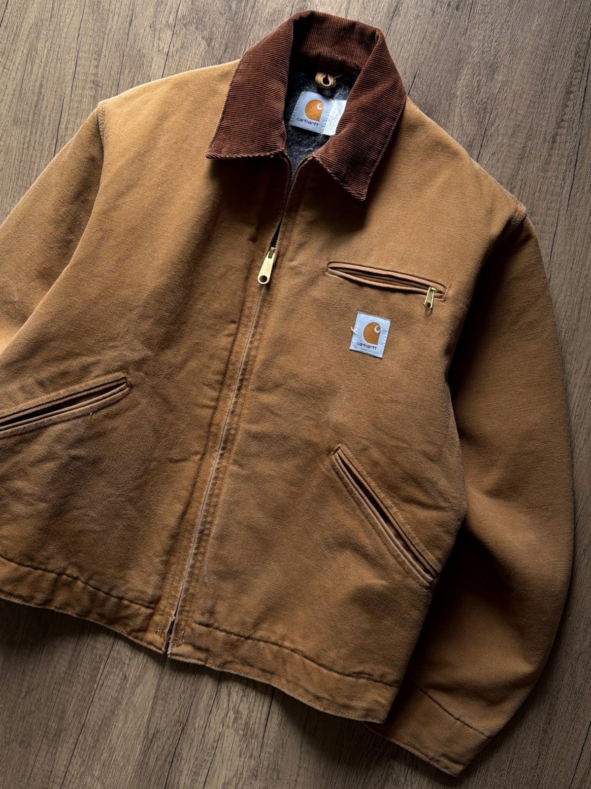 Brown corduroy Carhartt jacket with a dark collar laid on a wooden floor