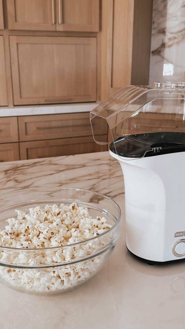 White electric popcorn maker and a glass bowl of popcorn on marble counter