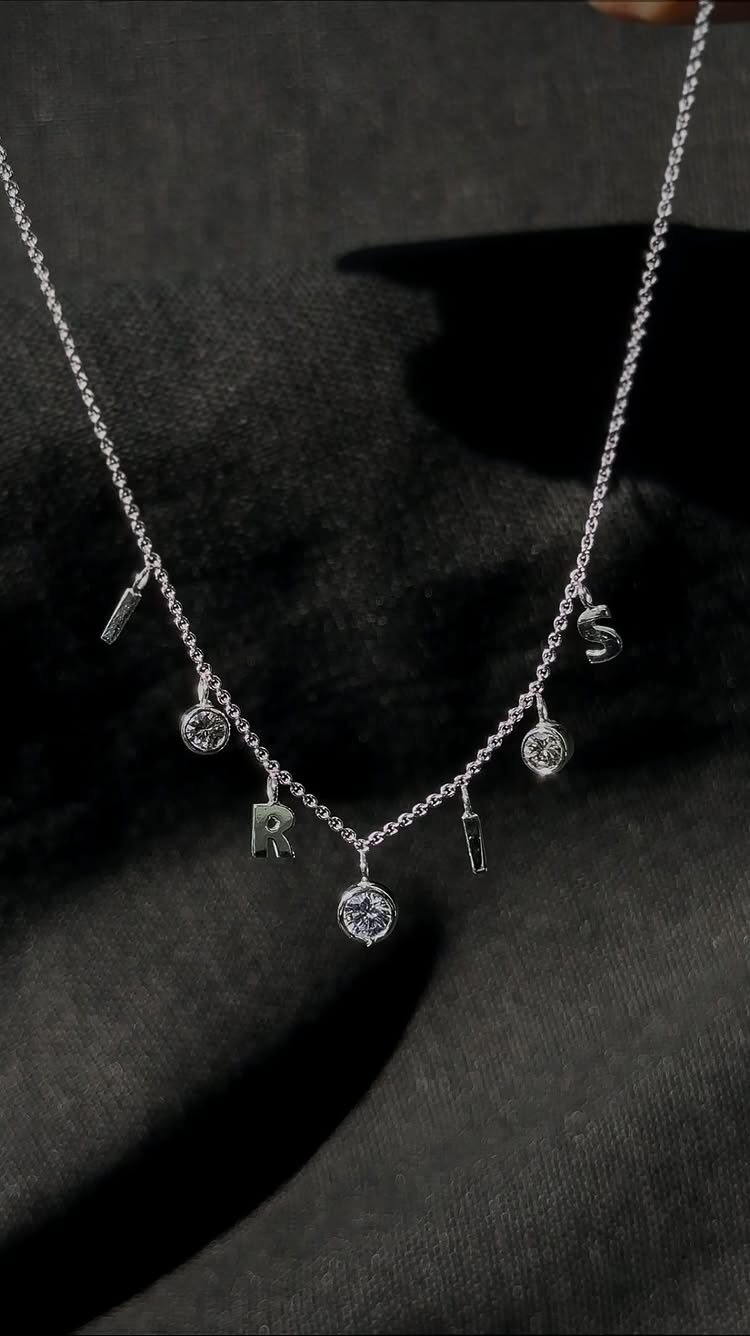 Silver chain necklace with letter charms and gemstones on black fabric background