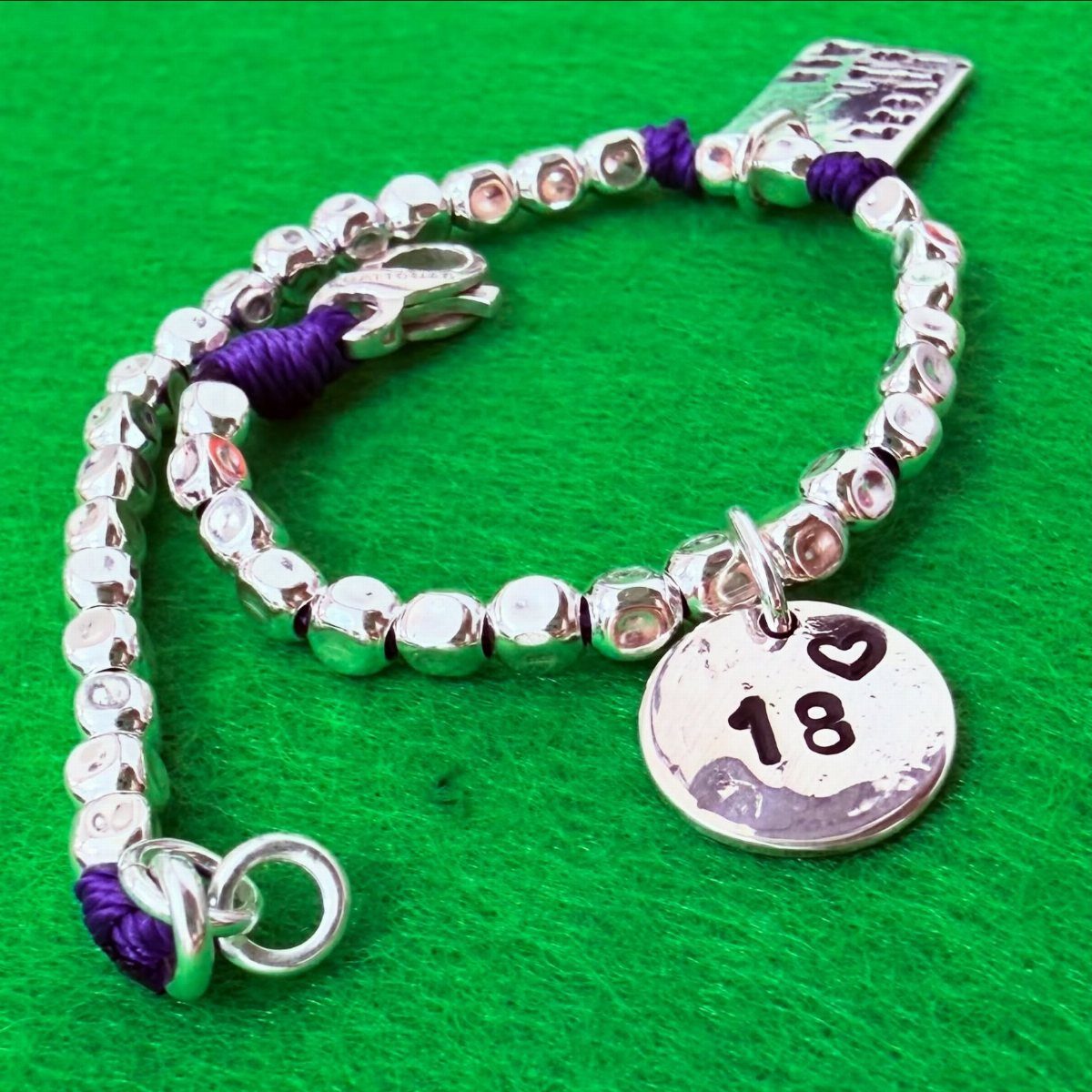 Silver beaded bracelet with a round charm engraved with 18 and a heart.