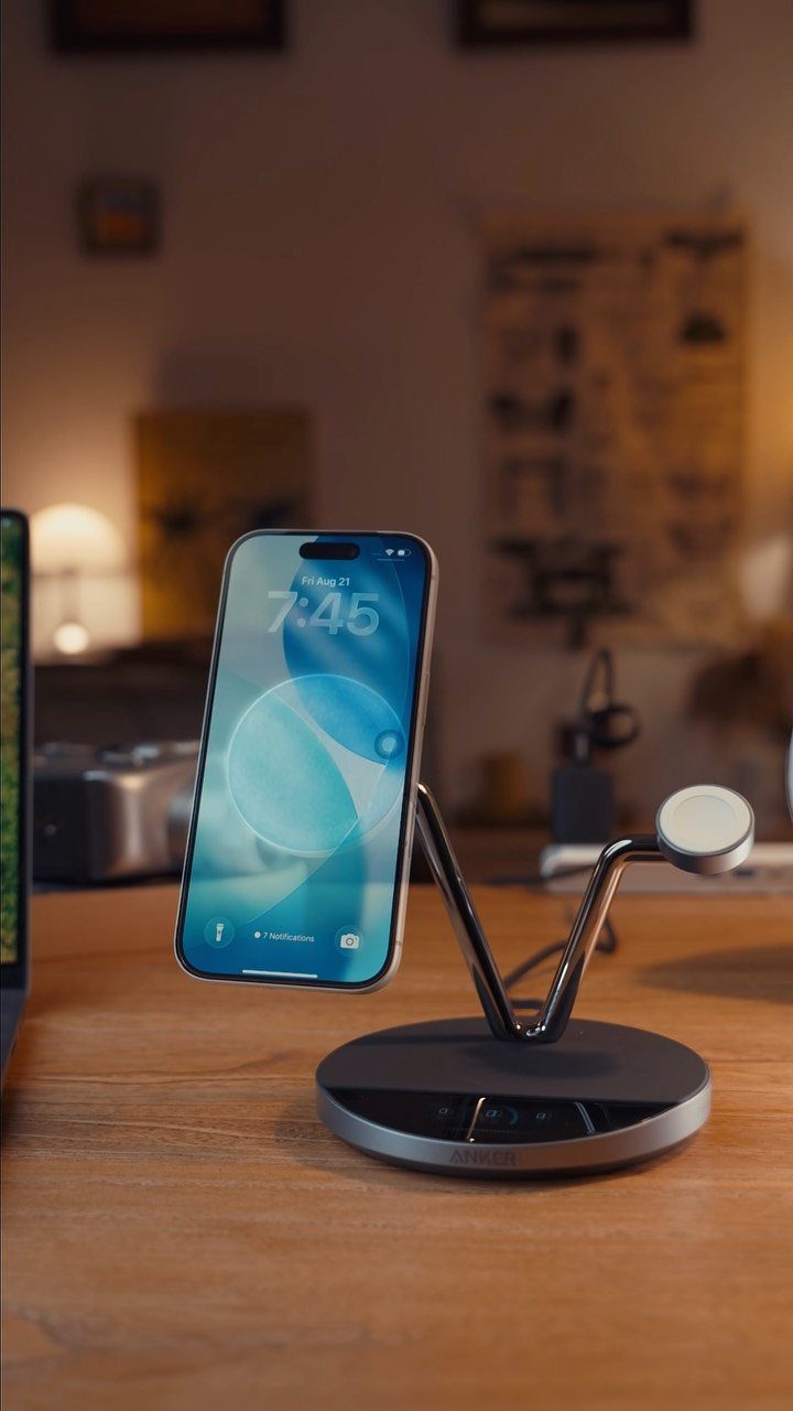 Smartphone resting on a modern metallic wireless charging stand on a wooden desk.