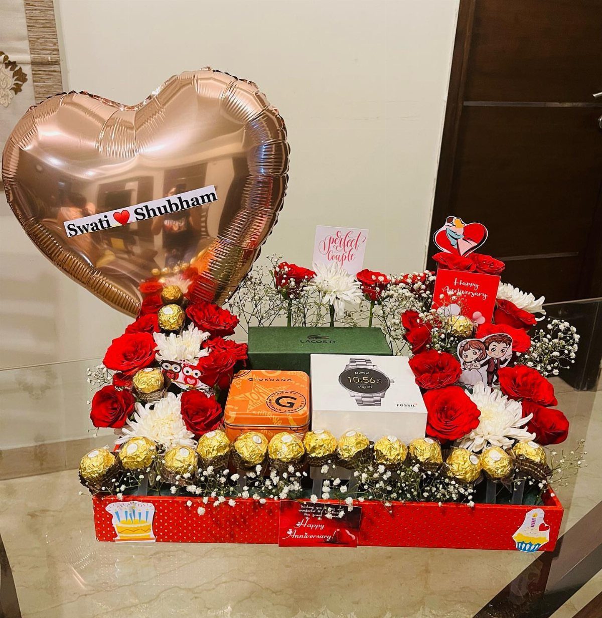 Gift hamper with red roses, chocolates, a watch, and a heart balloon.