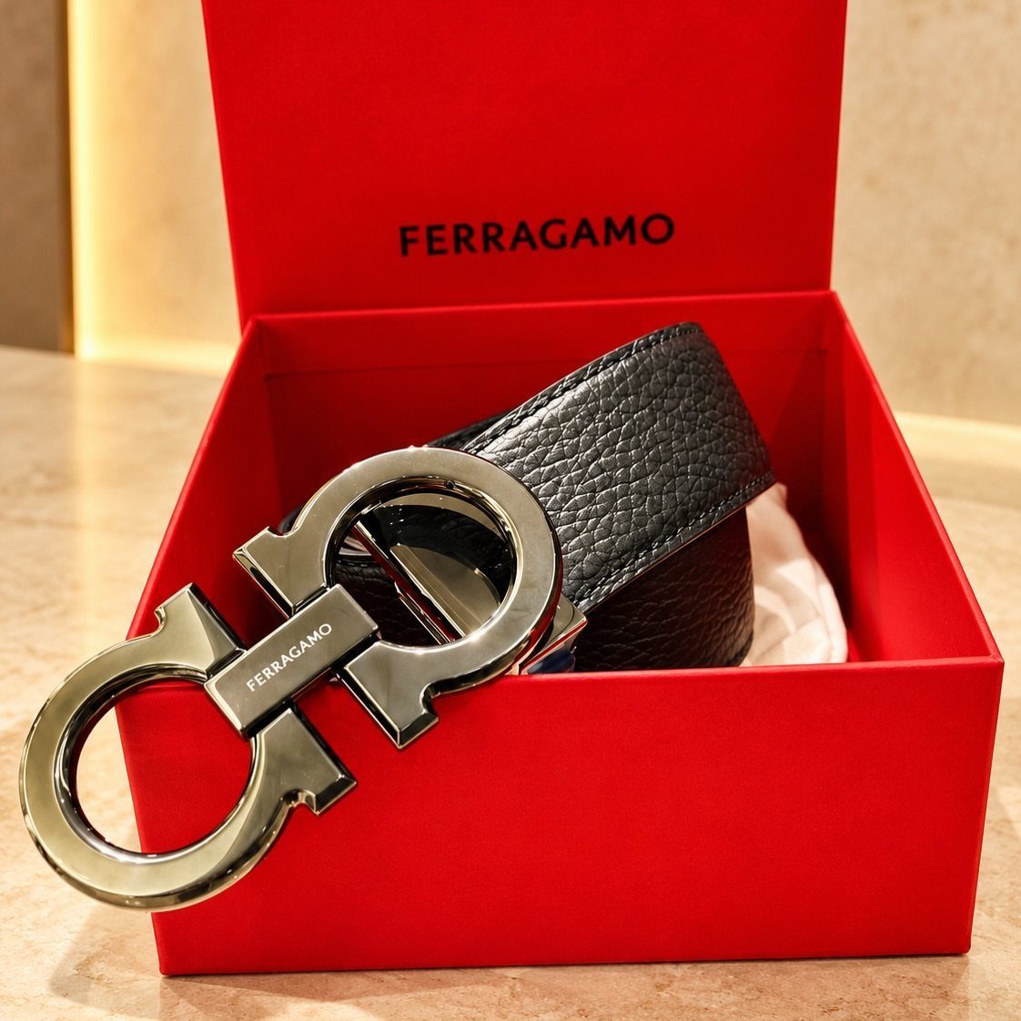 Black leather belt with silver buckle inside a red Ferragamo gift box