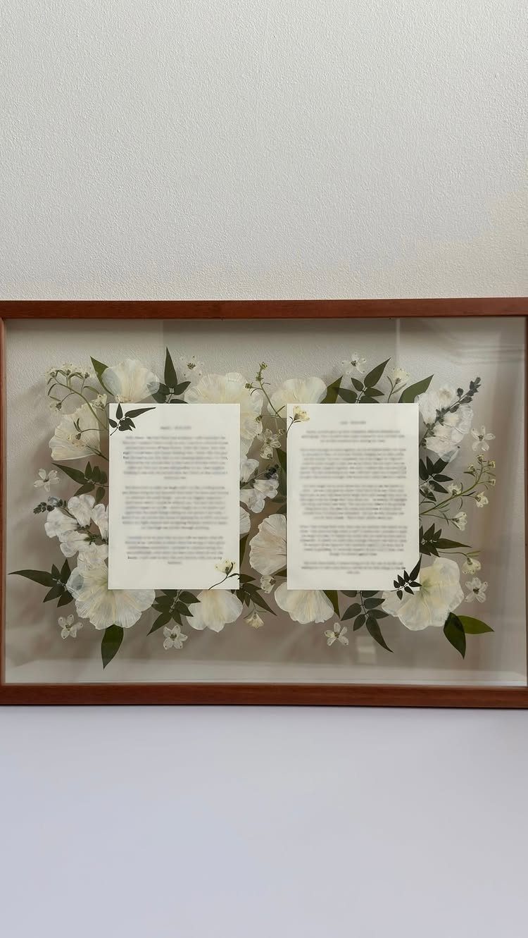 Framed wedding vows decorated with white flowers and green leaves on a wall