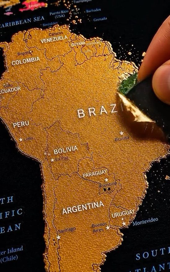 Gold scratch-off travel map of South America being scratched to reveal green colors.