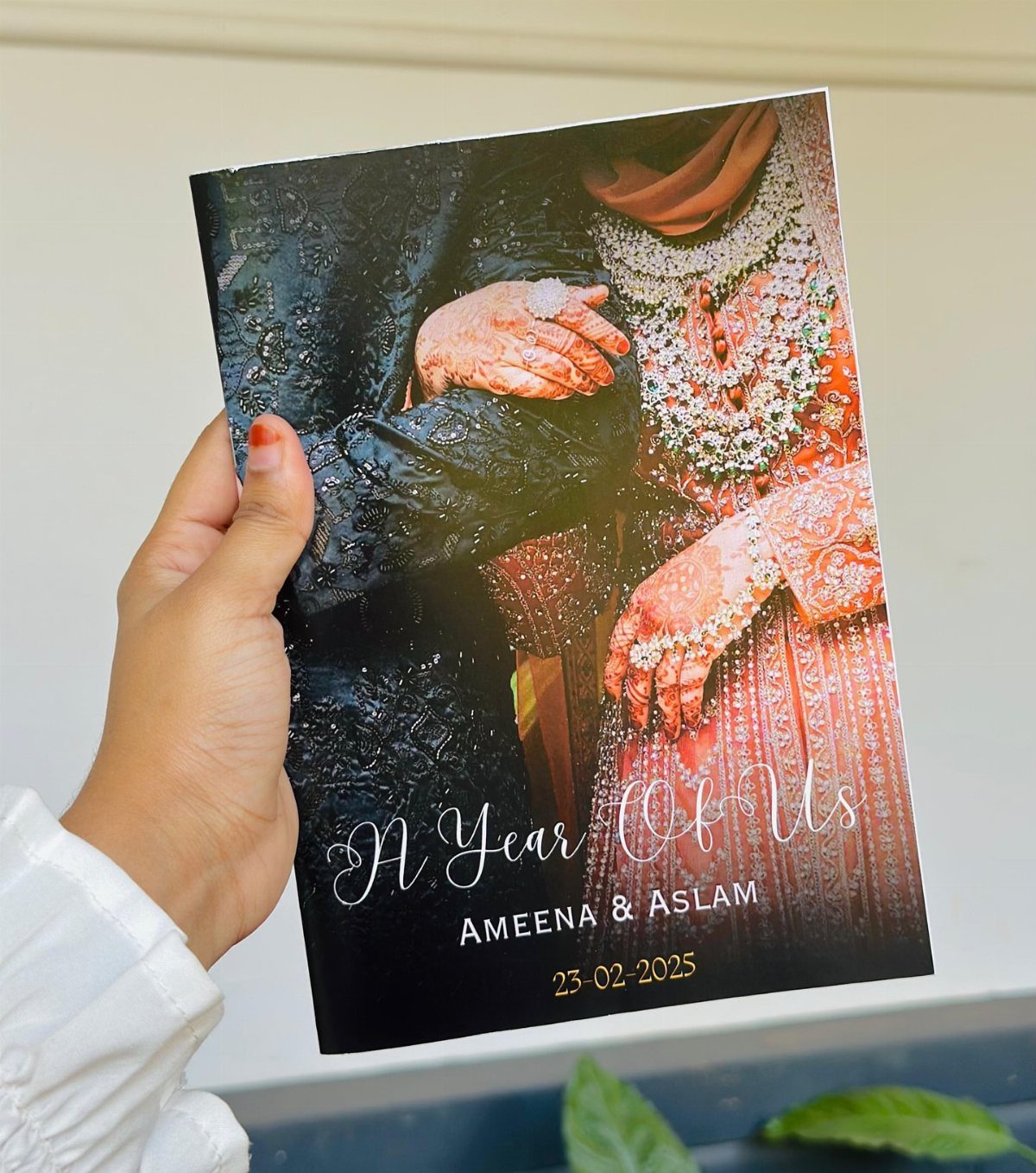 Wedding photo album cover held by a hand, featuring a couple and anniversary text.