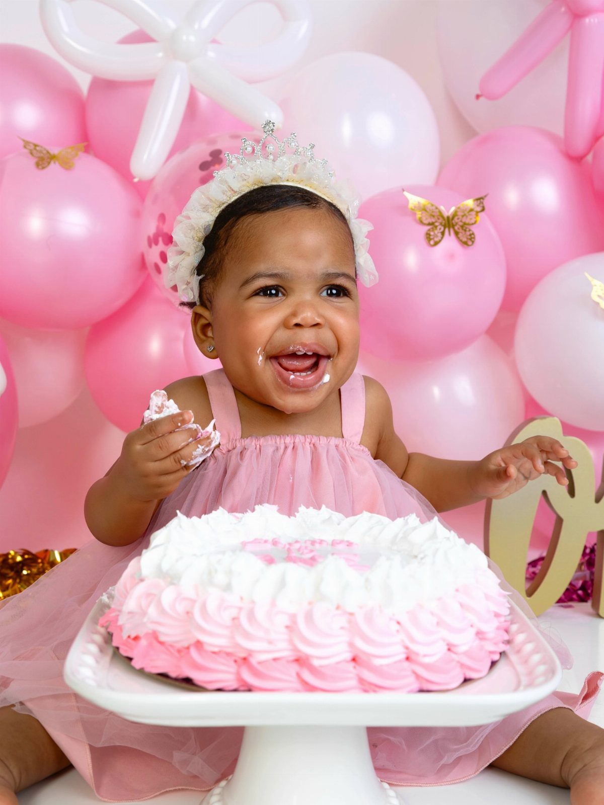 Baby girl in pink dress and tiara smiling with a pink smash cake.