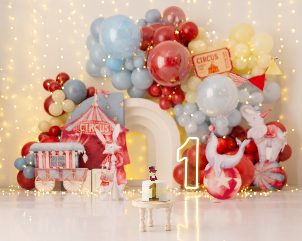 Circus themed birthday setup with balloons, a small cake, and a glowing number one.