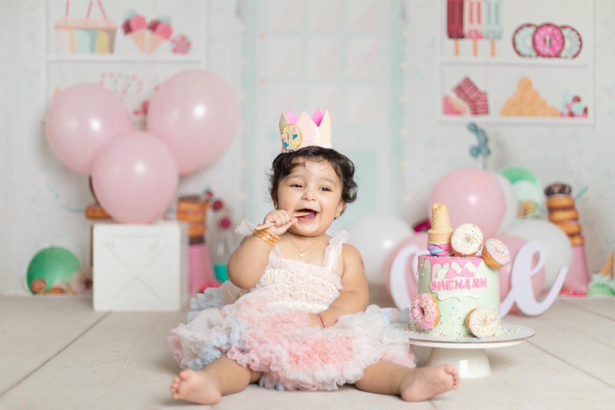 Baby girl in a tutu sitting next to a donut decorated smash cake.