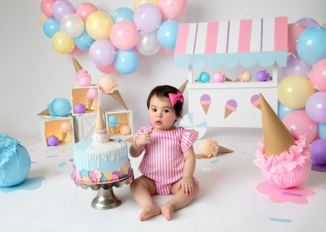 Baby girl sitting next to a blue cake in an ice cream parlor setting.