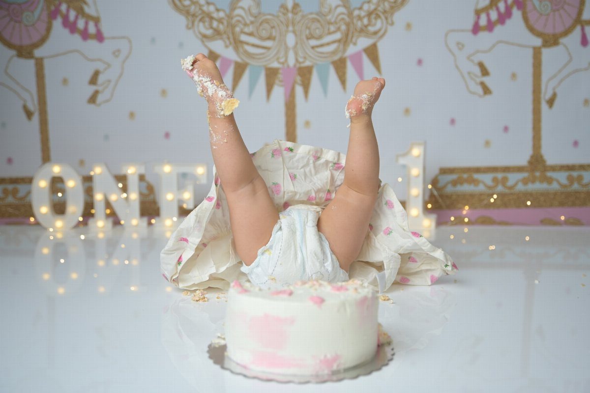 Baby face-down in a smash cake with legs in the air during photoshoot