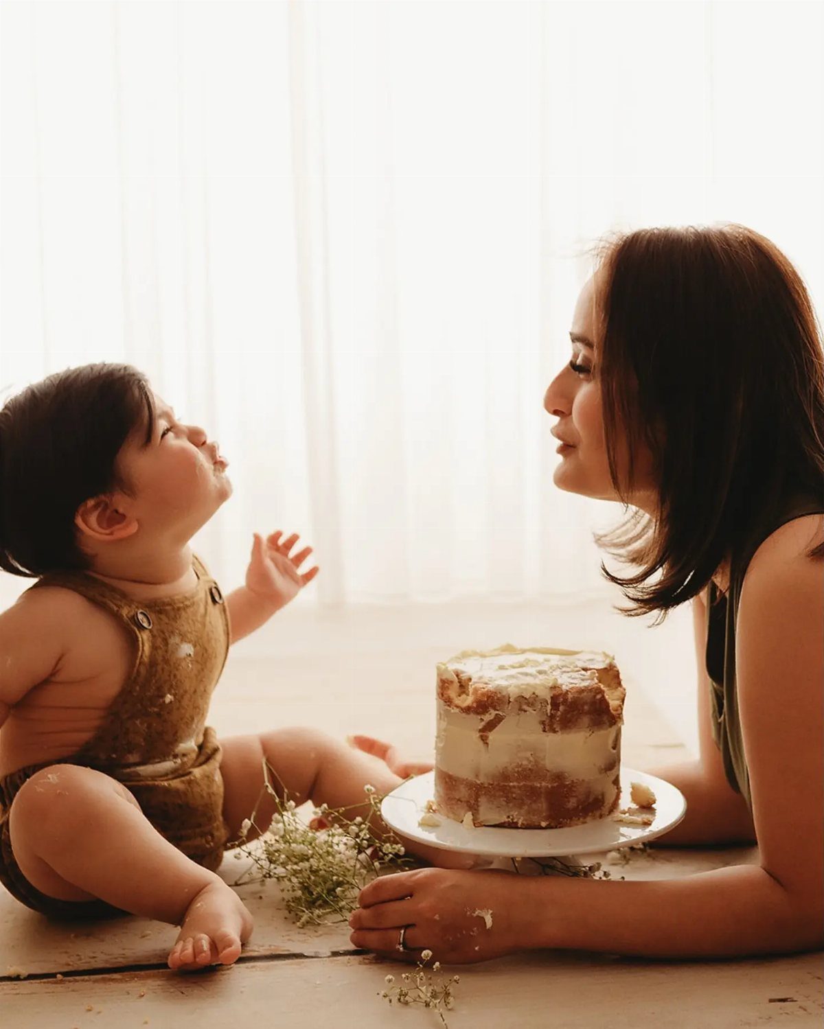 Baby and woman sitting on a floor with a small white smash cake.