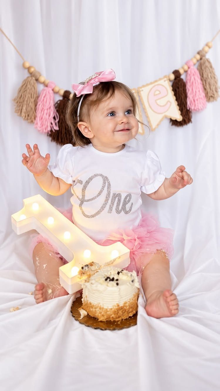 Baby girl in a white shirt and pink tutu with a smash cake.