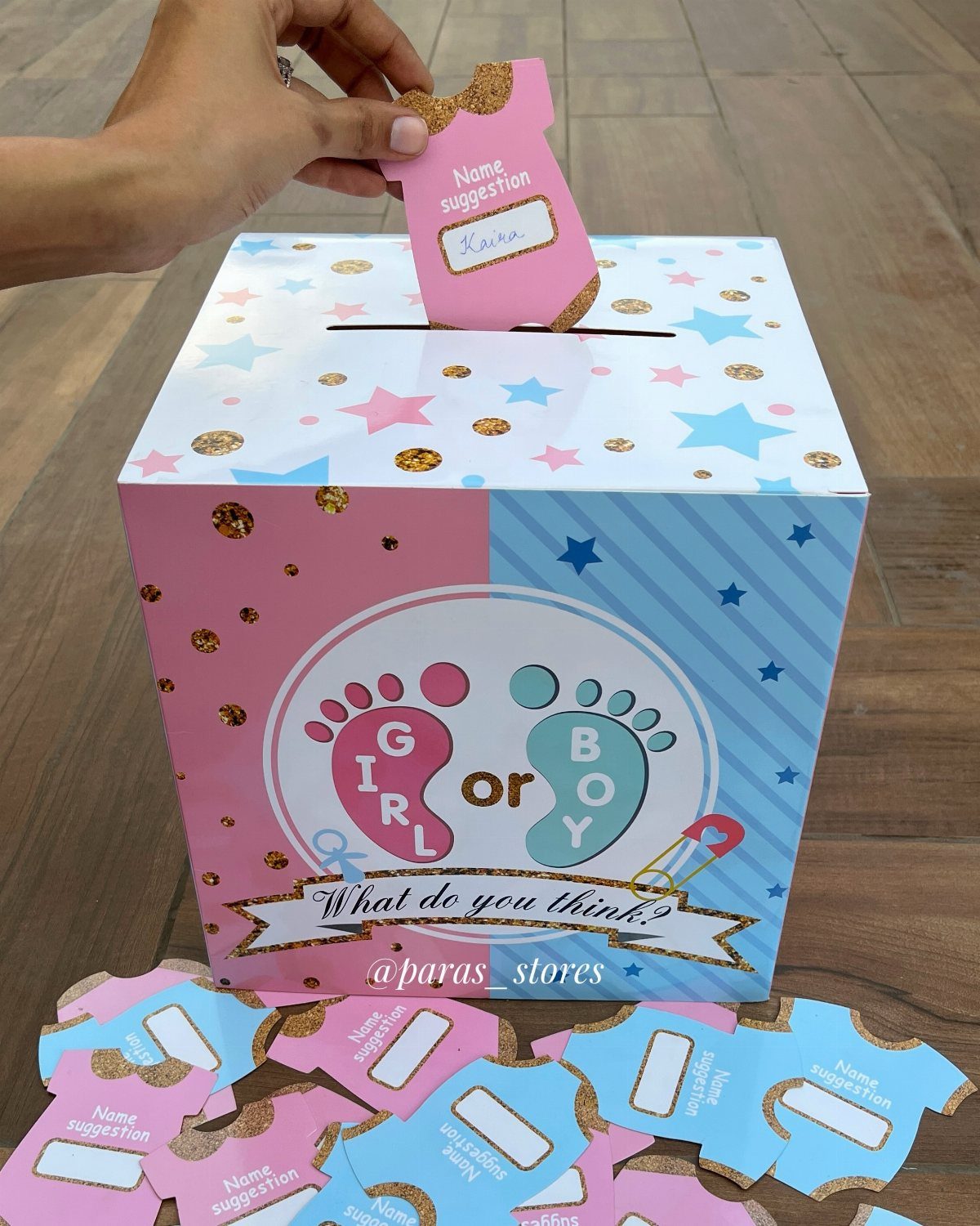 Hand placing a name suggestion slip into a pink and blue gender reveal box.