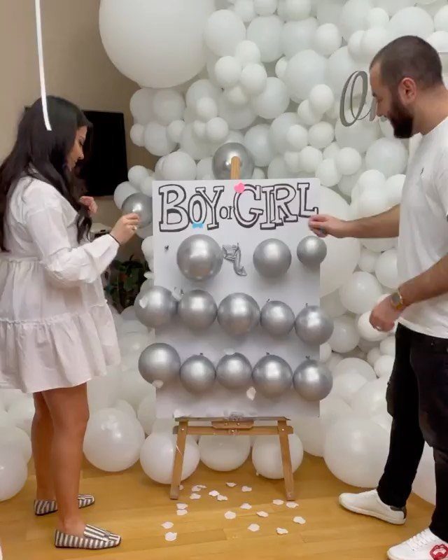 Couple popping silver balloons on a Boy or Girl board for gender reveal