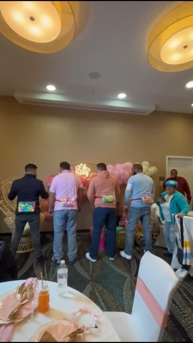 Four men with balloons tucked into their waistbands simulating pregnancy bellies at a party.
