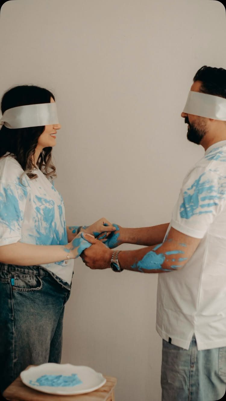 Blindfolded couple covered in blue paint holding hands during a gender reveal activity.