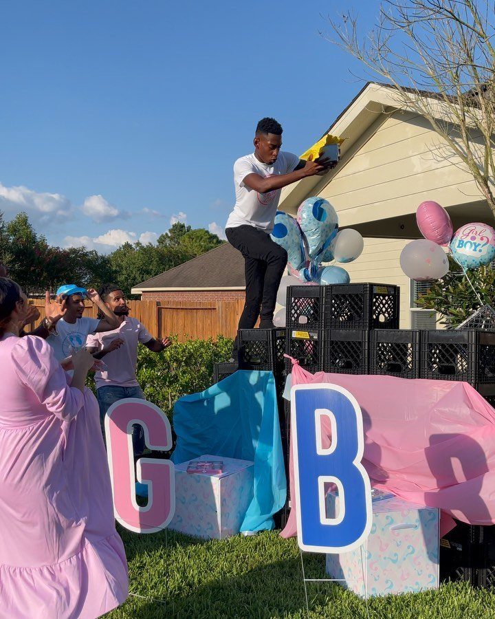 Man standing on black crates at a gender reveal party with balloons.