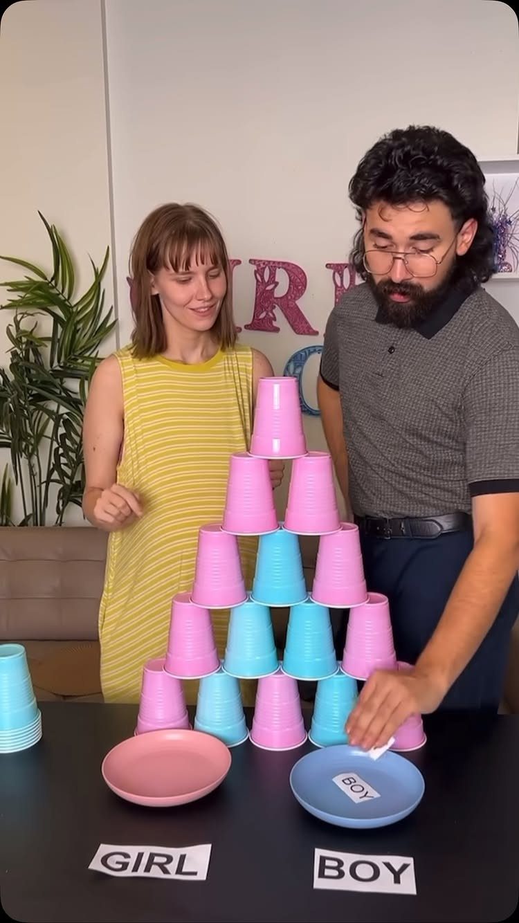 Man and woman with a pyramid of pink and blue cups for gender prediction.
