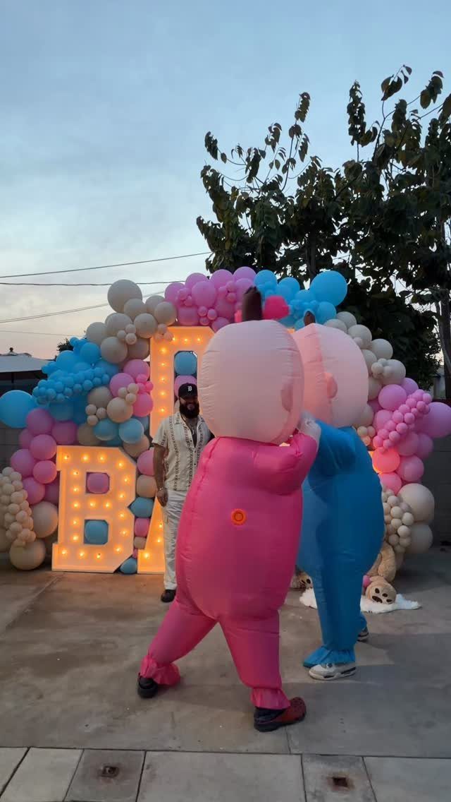 Two people in pink and blue inflatable sumo suits at a gender reveal party.