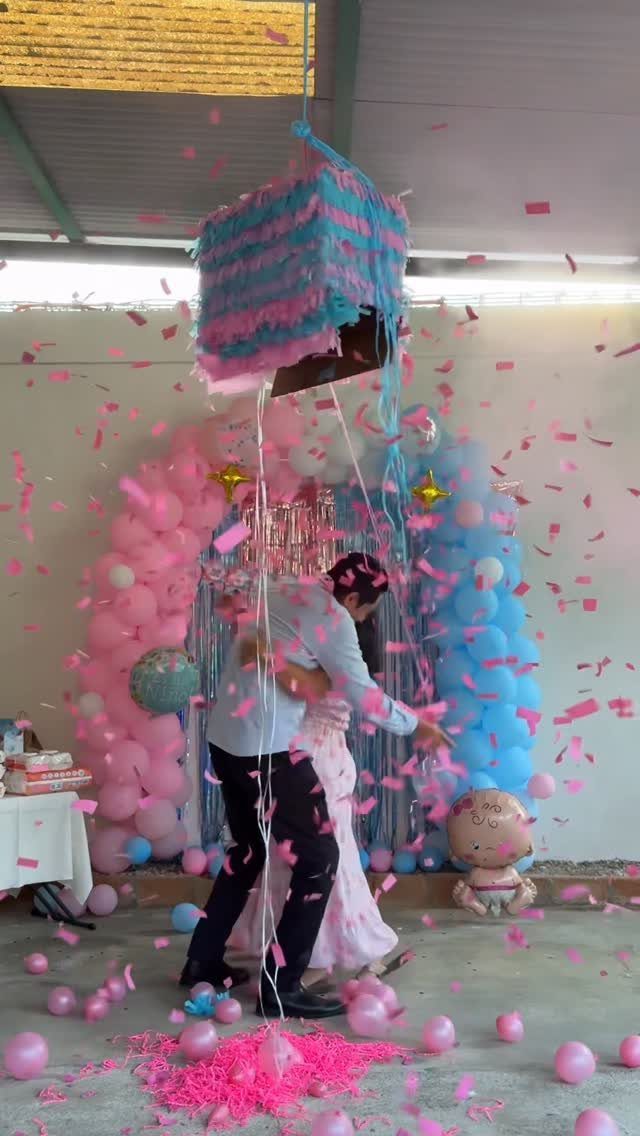 Couple embracing as pink confetti falls from a blue and pink piñata.