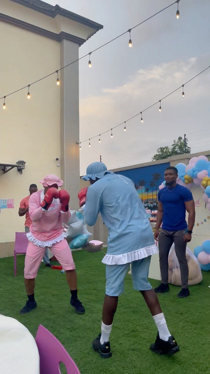 Two men in pink and blue boxing gear and skirts boxing at a party.