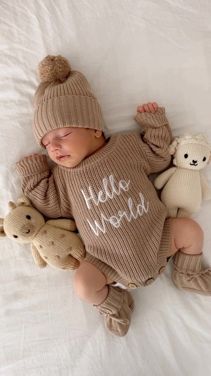 Sleeping newborn baby in a tan ribbed knit outfit and beanie on white bedding.