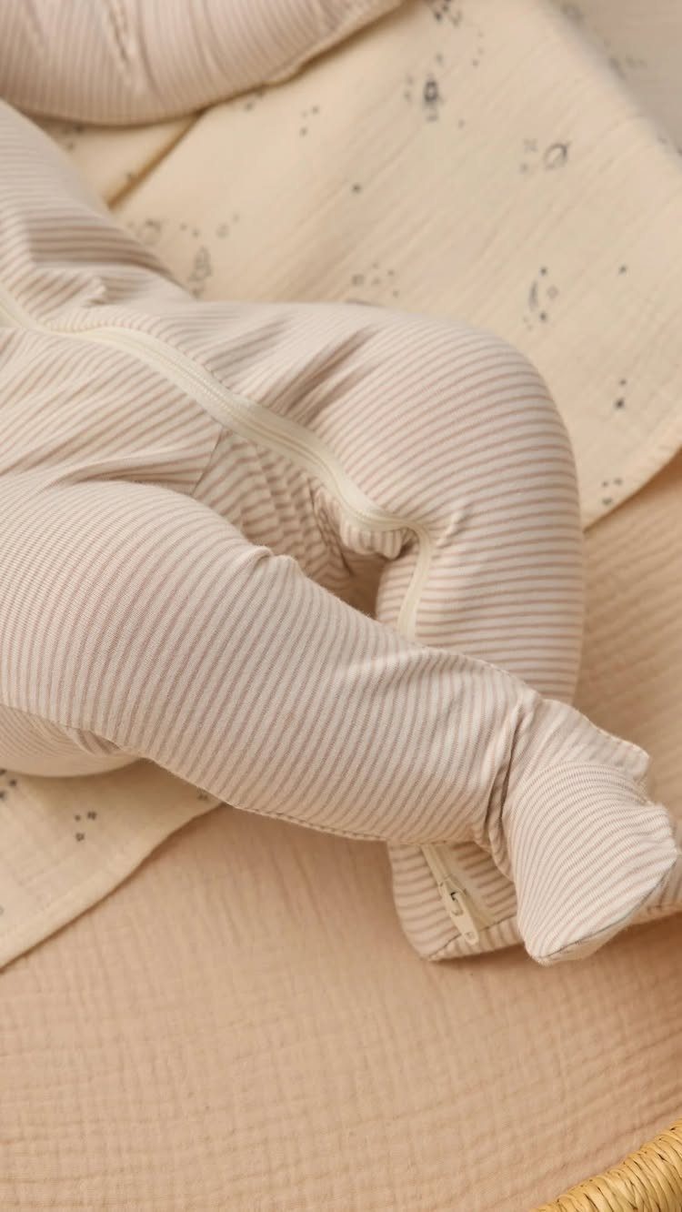 Newborn baby in a beige striped footed sleeper lying on a cream blanket.