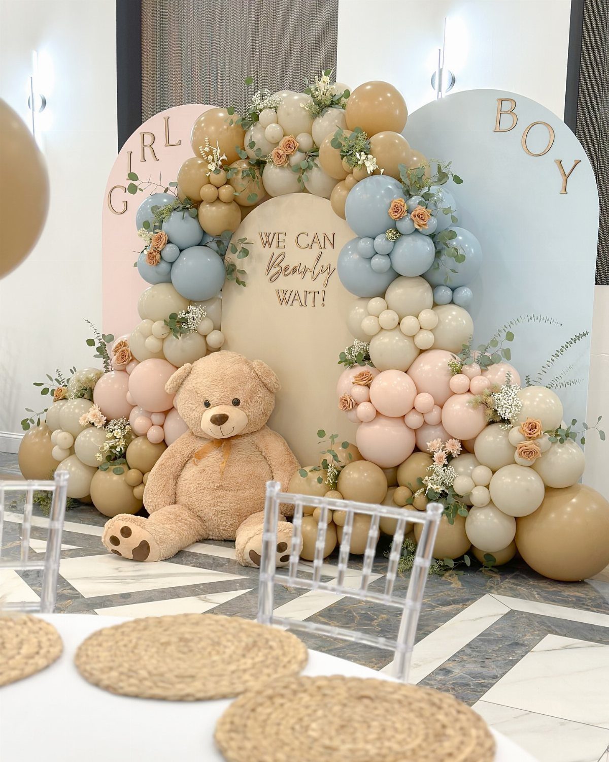 Teddy bear sitting before a balloon arch and gender reveal backdrop panels.