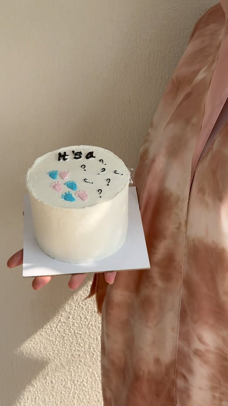 Small white gender reveal cake with pink and blue accents and question marks.