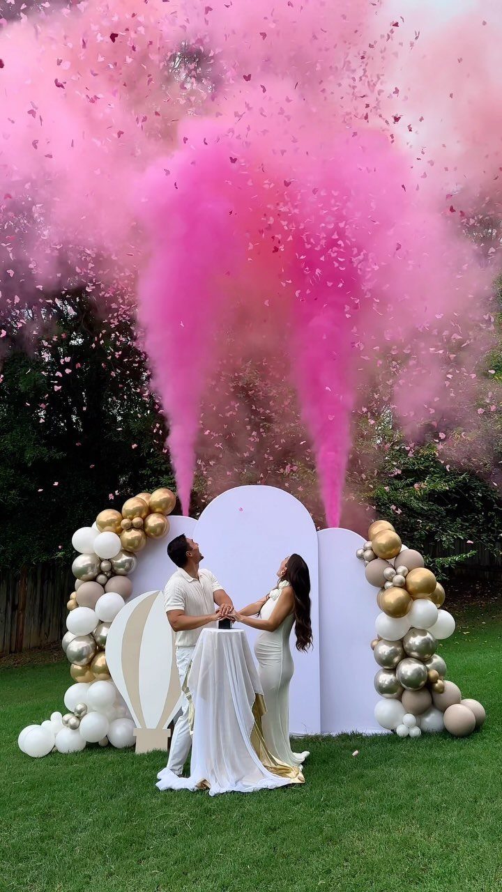 Couple standing before balloon decor as pink confetti and smoke erupt upwards.