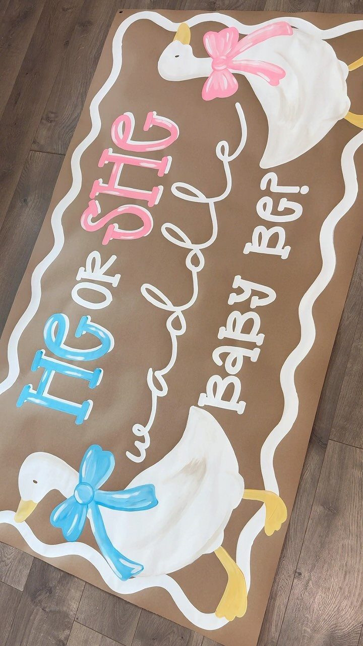 Brown gender reveal banner with ducks and text on a wooden floor