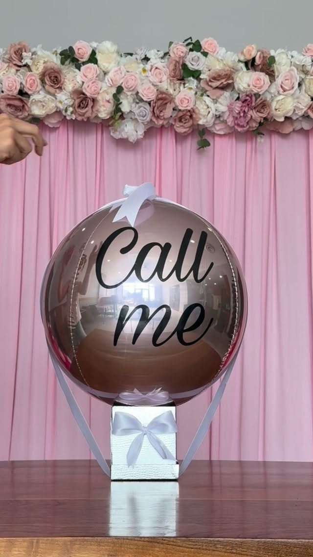 Clear balloon with 'Call me' text and rose gold interior on a gift box.