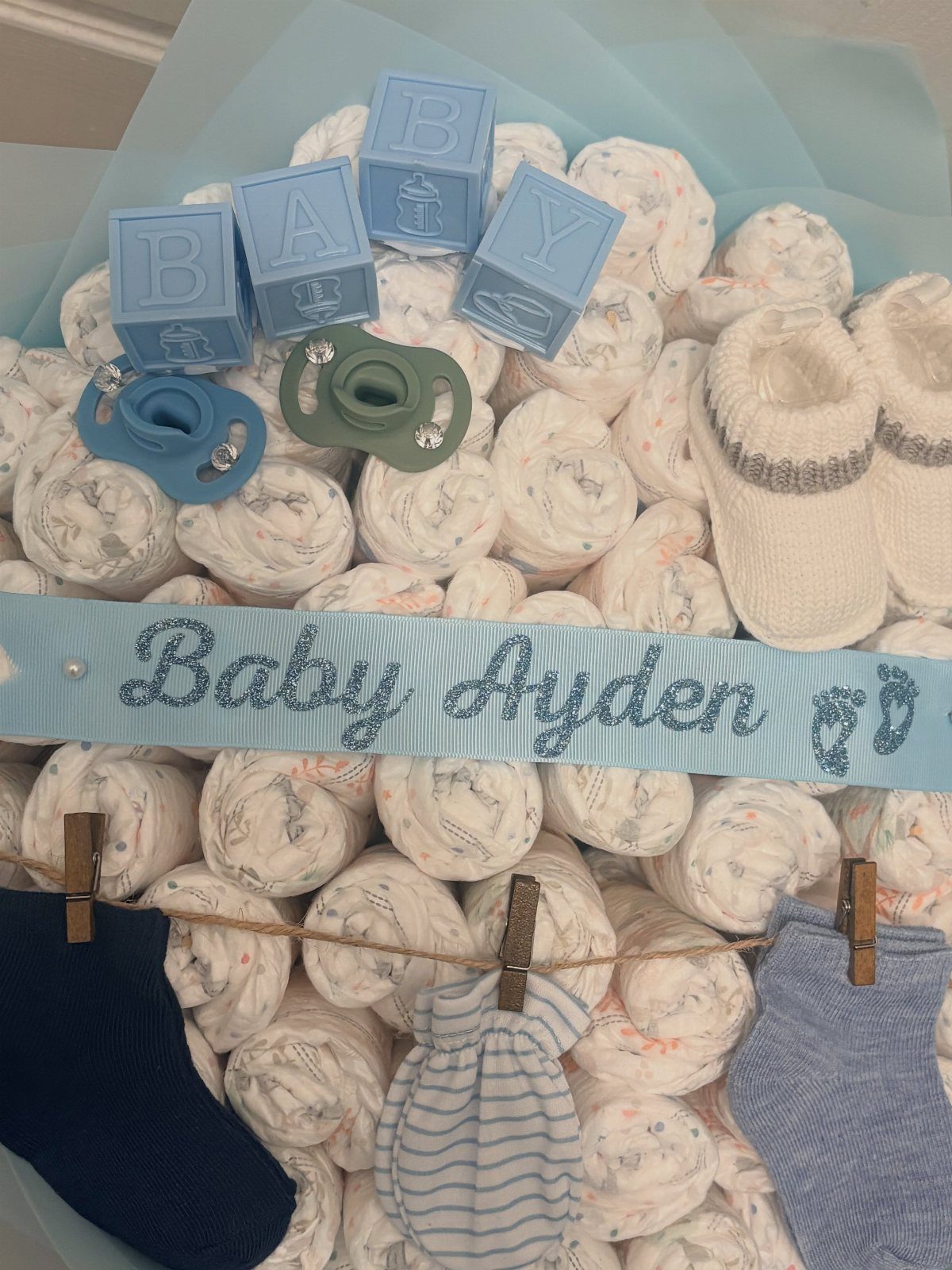 Diaper cake gift with blue baby blocks, pacifiers, booties, and socks for Baby Ayden.