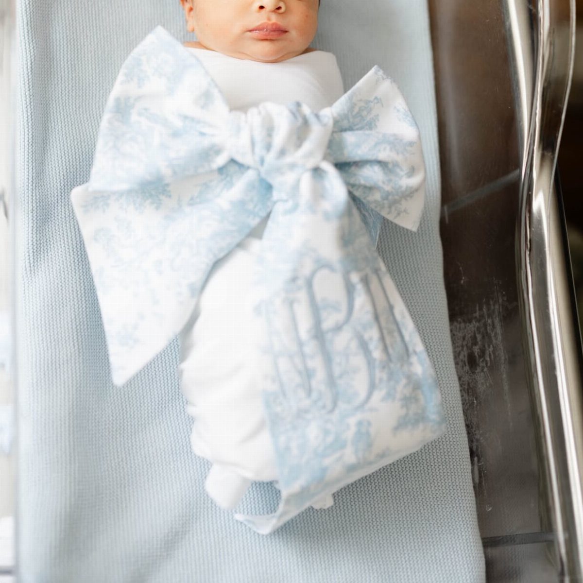 Newborn baby wrapped in a light blue monogrammed swaddle blanket tied in a bow.