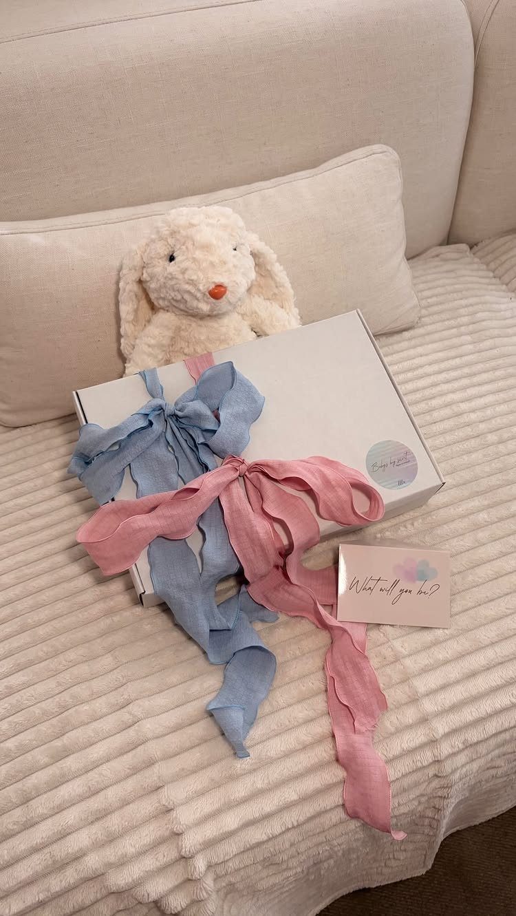 White gift box with pink and blue ribbons next to a plush bunny
