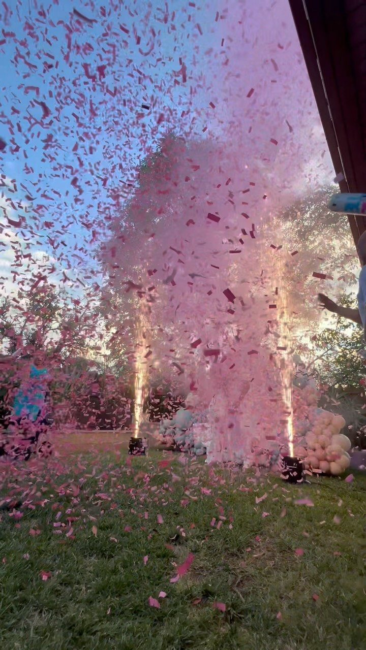 Pink confetti and sparks erupting outdoors with pink and white balloons in background