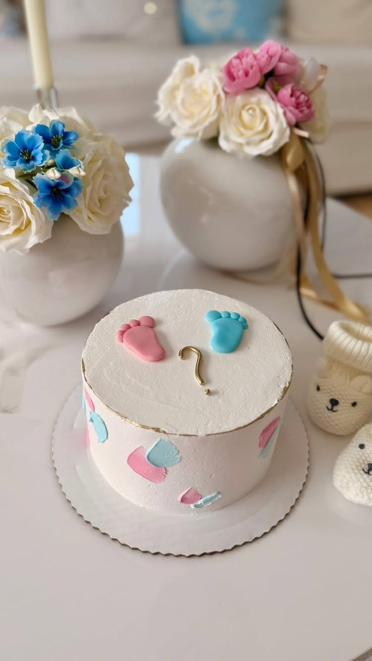 White gender reveal cake with pink and blue footprints and a gold question mark.