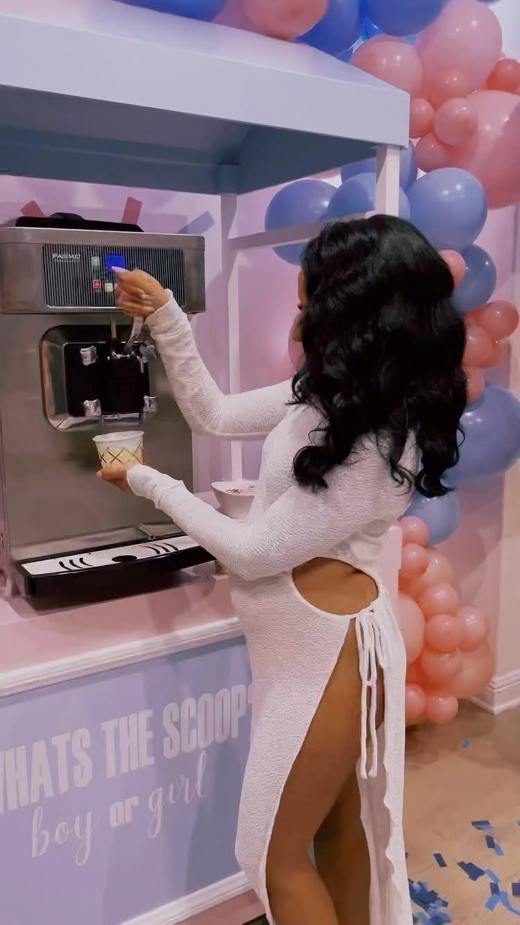 Woman using soft-serve ice cream machine at a gender reveal party with balloons.