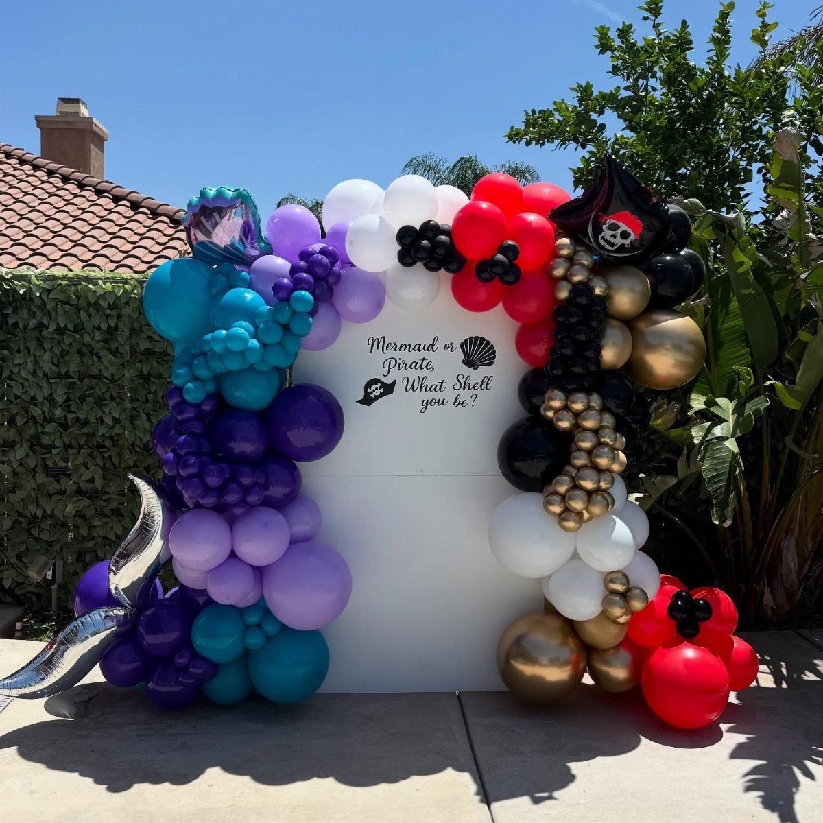 Balloon arch backdrop with mermaid and pirate themes for a gender reveal party
