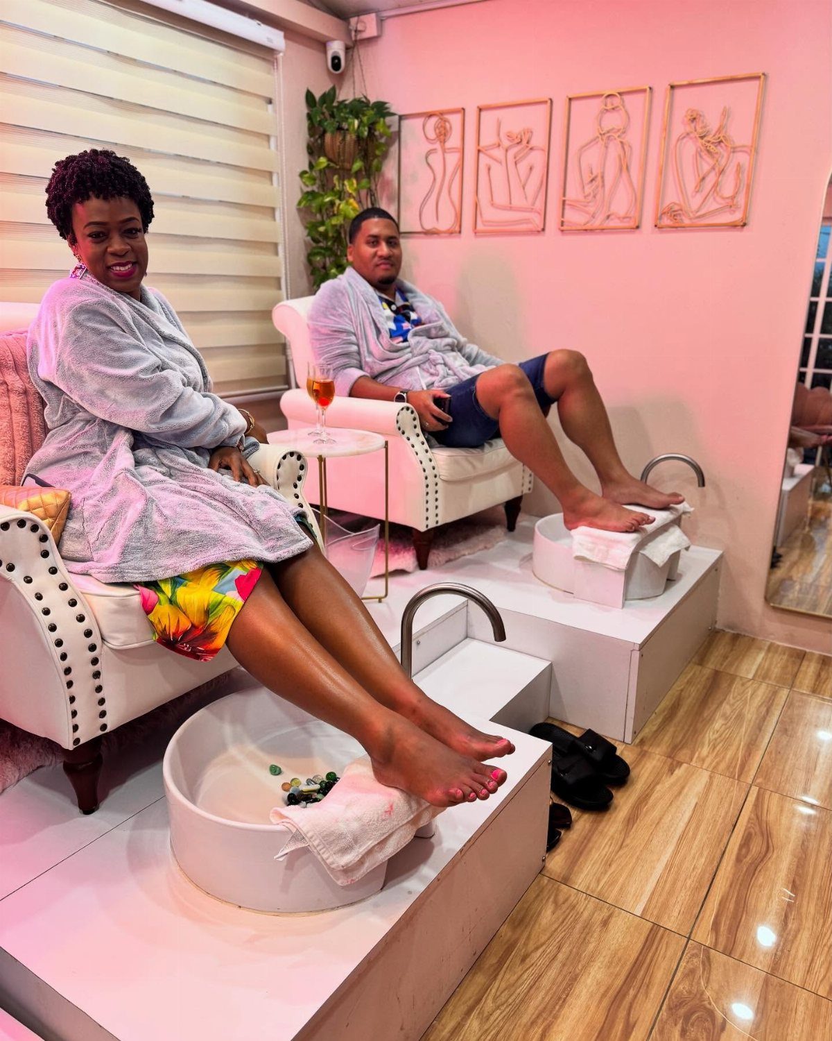 Couple in grey robes relaxing in white pedicure chairs at a spa.