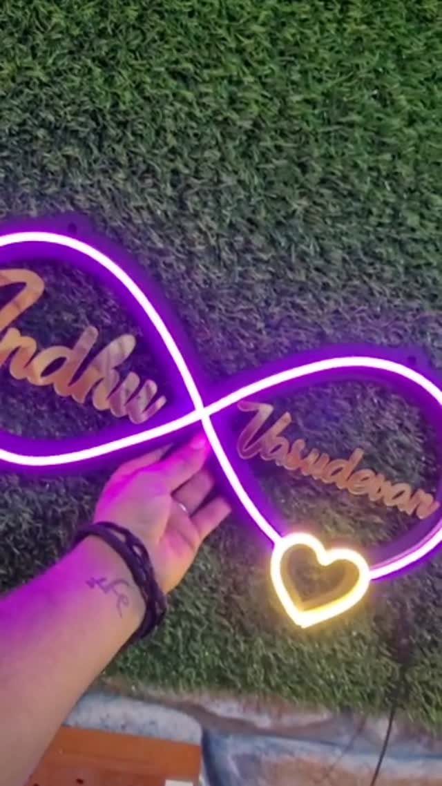 Purple neon infinity sign with names and a heart held against green foliage