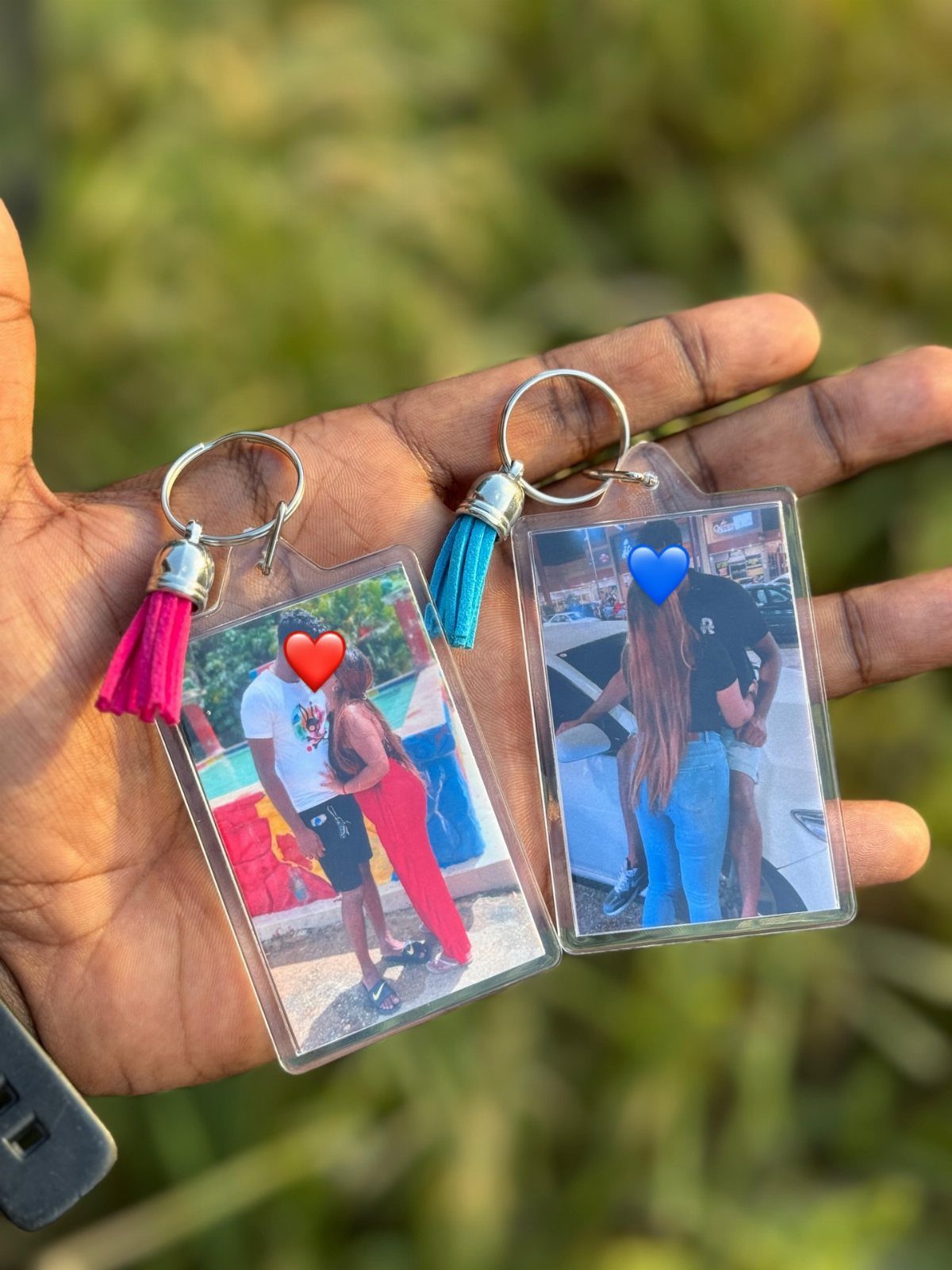 Two acrylic photo keychains with tassels held in a hand outdoors.