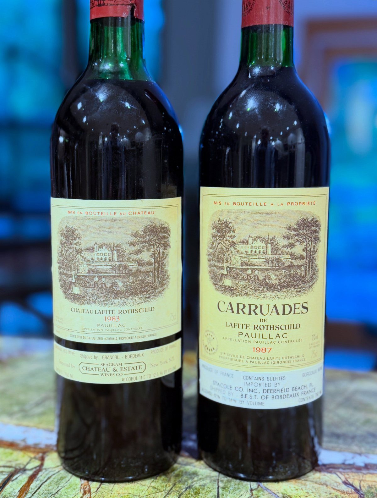Two vintage wine bottles with chateau labels standing on a rustic wooden surface.